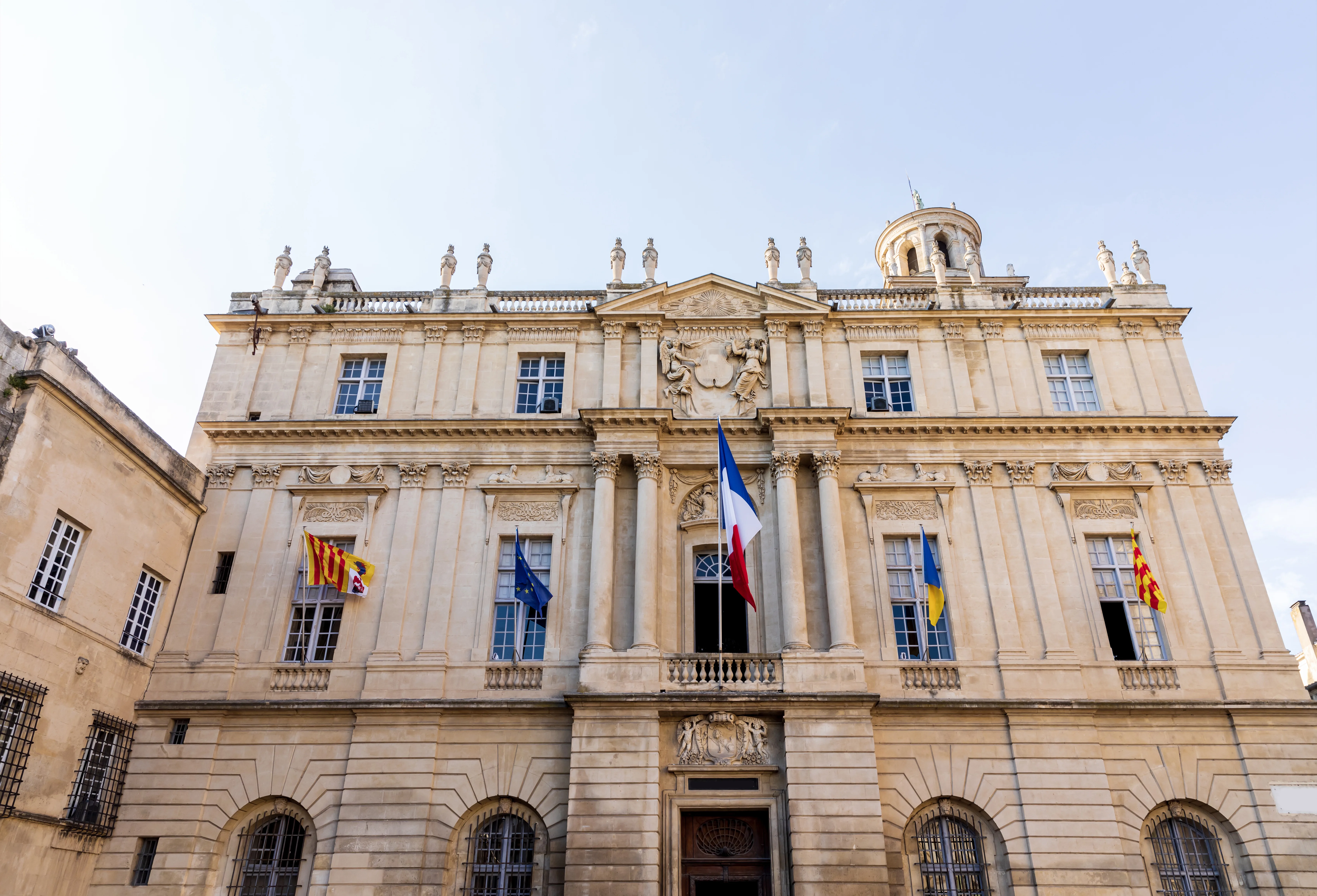 Façade d'un bâtiment de style classique avec des drapeaux, symbole des institutions locales