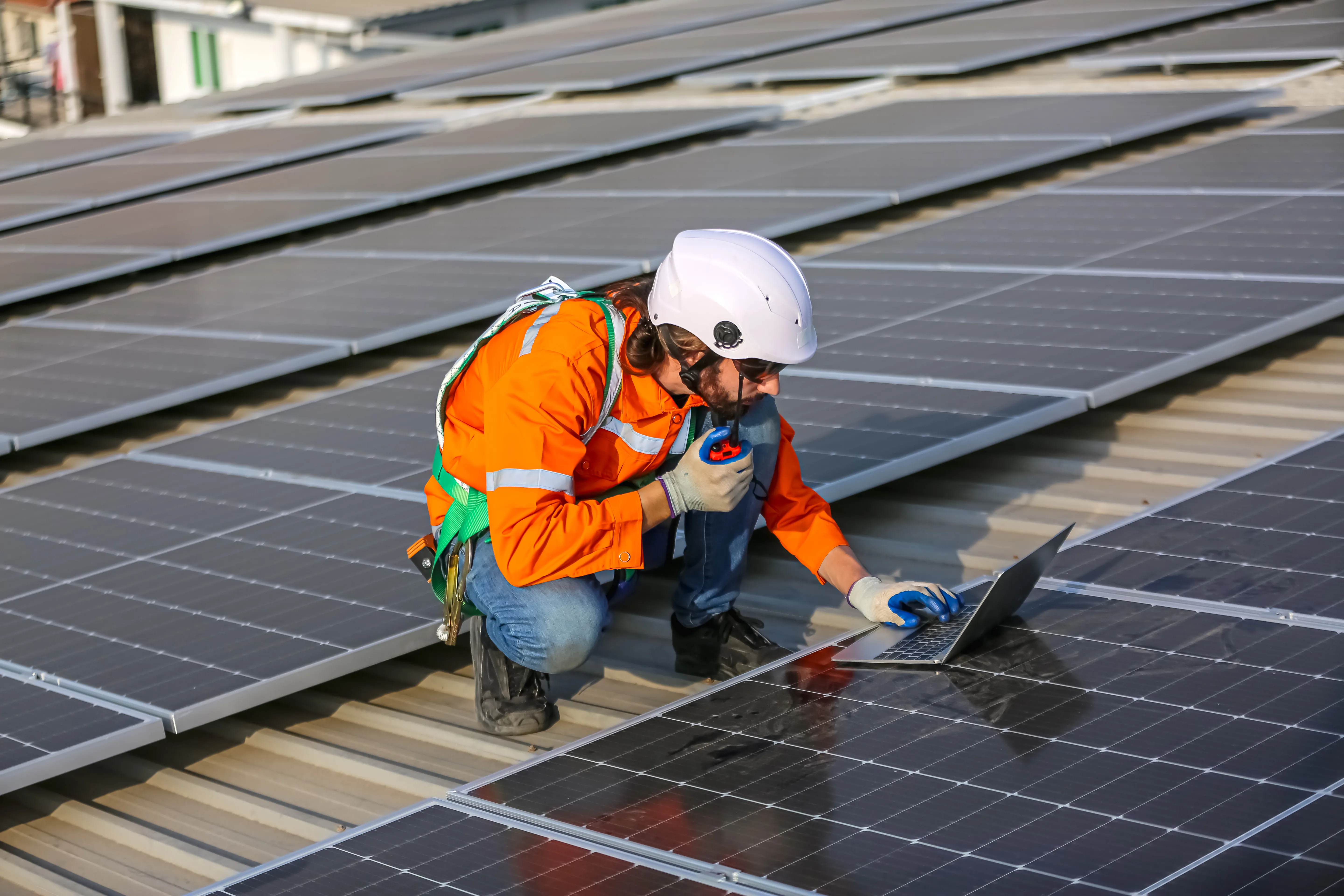 Technicien en maintenance de panneaux photovoltaïques sur un toit, utilisant un ordinateur portable