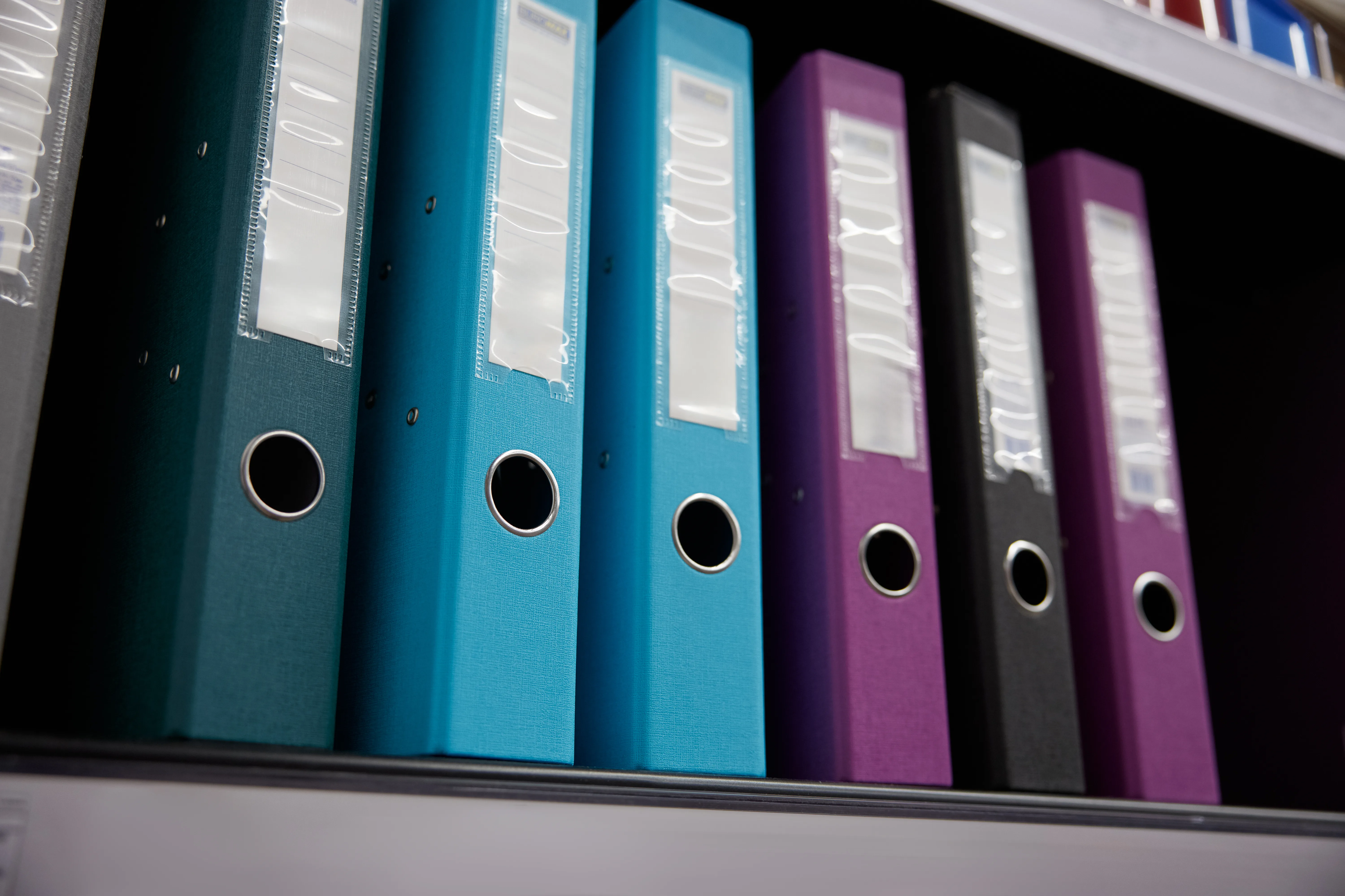 Dossiers de différentes couleurs rangés sur une étagère, reflétant l'organisation