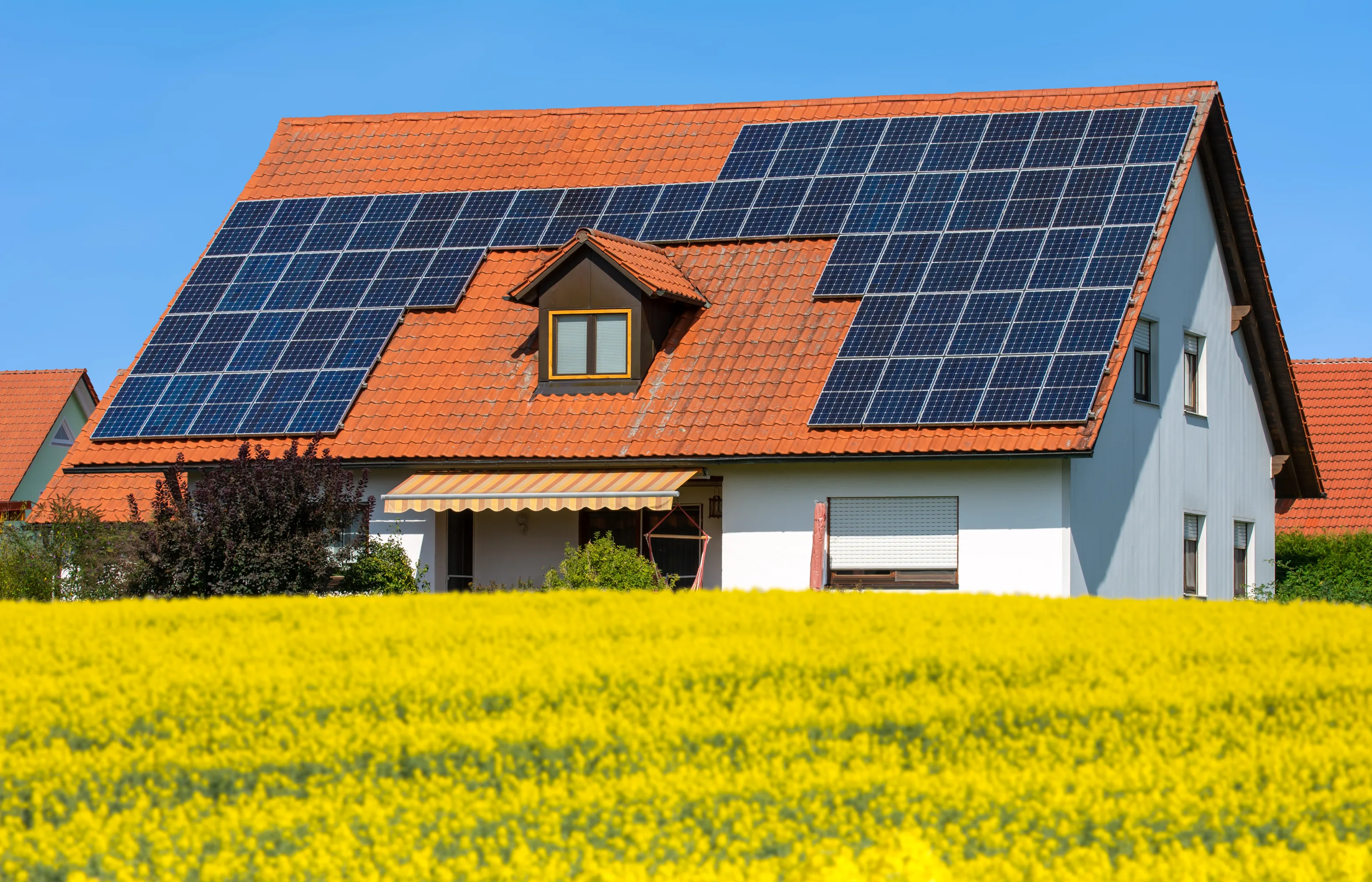 Installation de panneaux photovoltaïques sur le toit d'une maison avec un champ de fleurs jaunes au premier plan