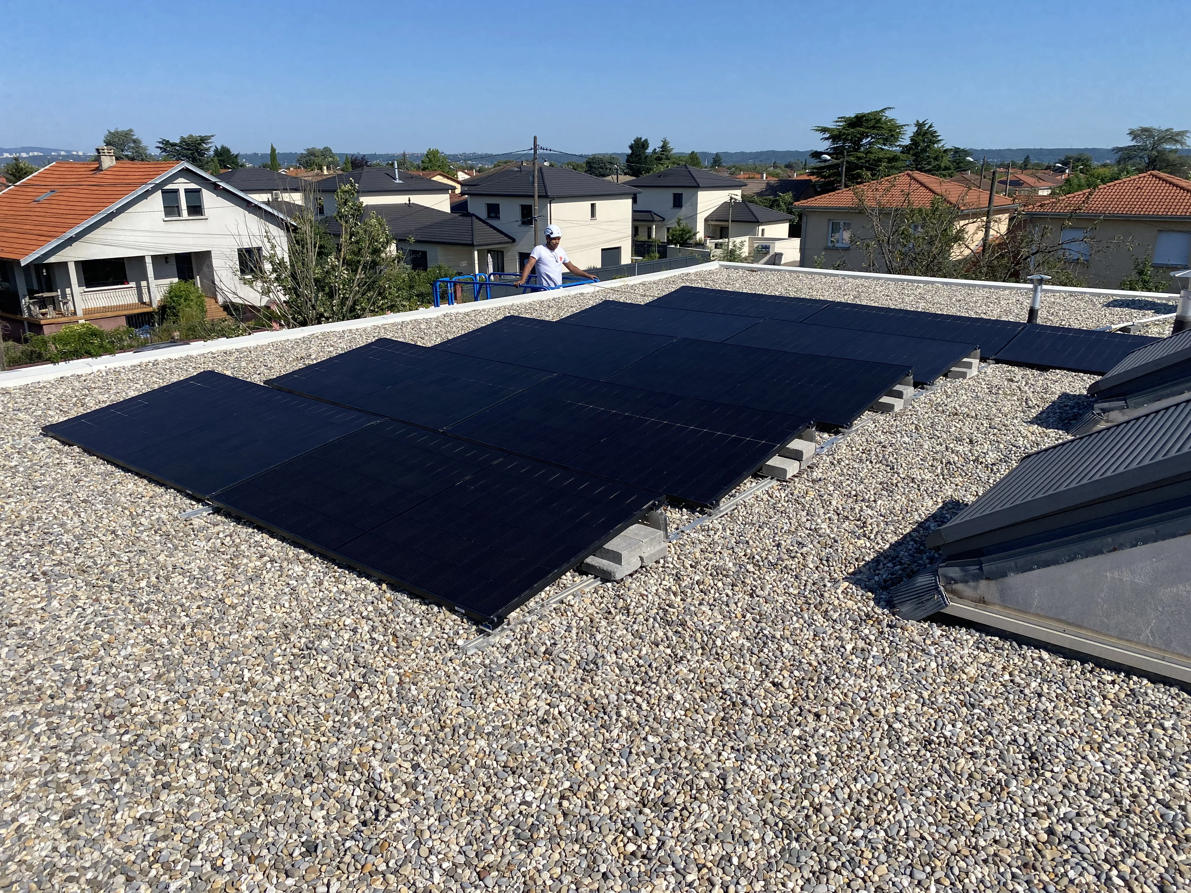 Installation de panneaux photovoltaïques sur un toit plat, avec vue sur des maisons environnantes